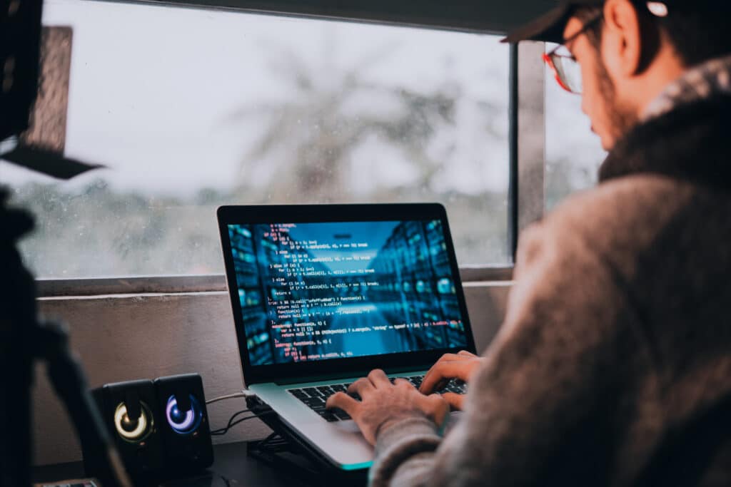 Développeur programme sur un laptop avec code bleu. Des haut-parleurs colorés et une fenêtre lumineuse en arrière-plan.