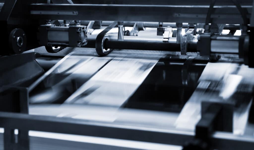 Machine d'impression industrielle en action. Des feuilles de papier traversent rapidement des rouleaux, créant un flou de mouvement. Tons bleutés.